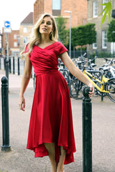 A woman wearing a cherry red silky satin special occasion dress with a flirty high-low hem and pleating.