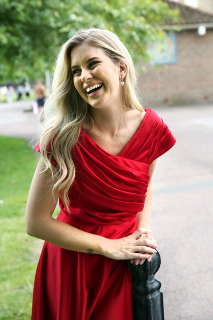 A woman wearing a cherry red silky satin special occasion dress with a flirty high-low hem and pleating.