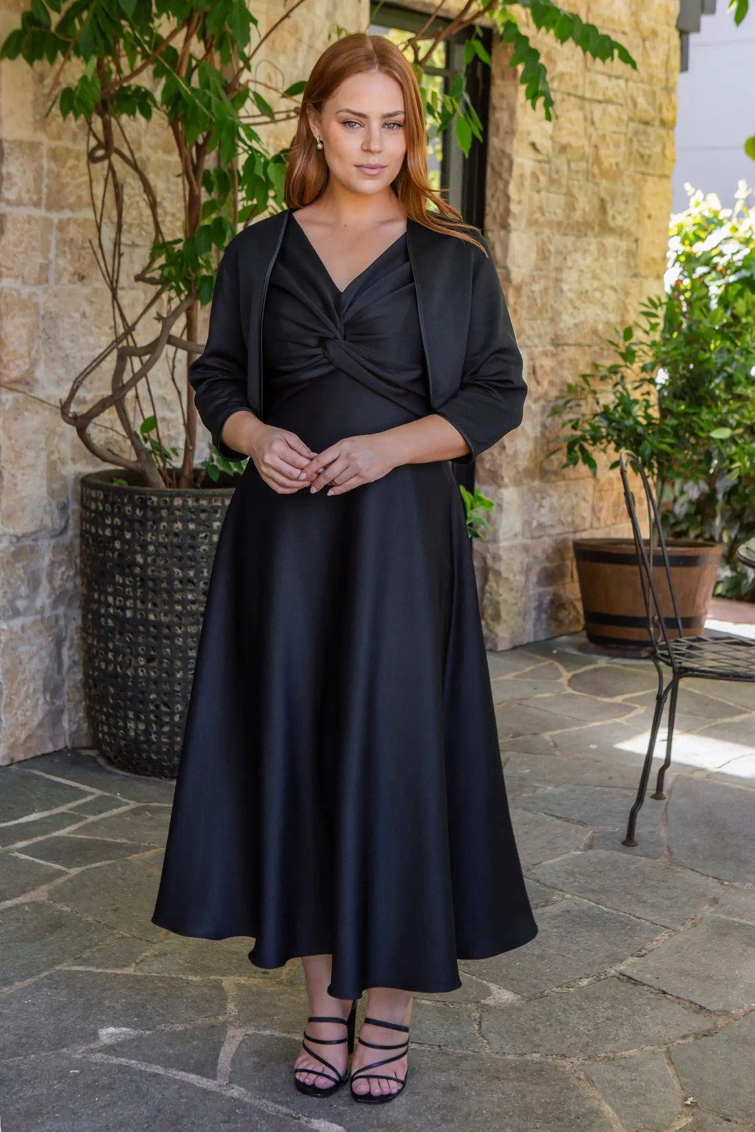 Woman wearing a black dress with a matching jacket outdoors.