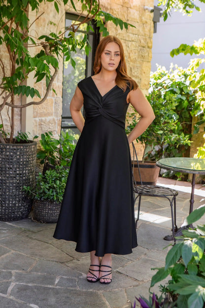 Woman in a black dress standing outdoors with plants and a table in the background