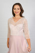 A woman models a blush-coloured, midi-length, beaded special occasion dress with a sweetheart neckline and 3/4 sleeves.