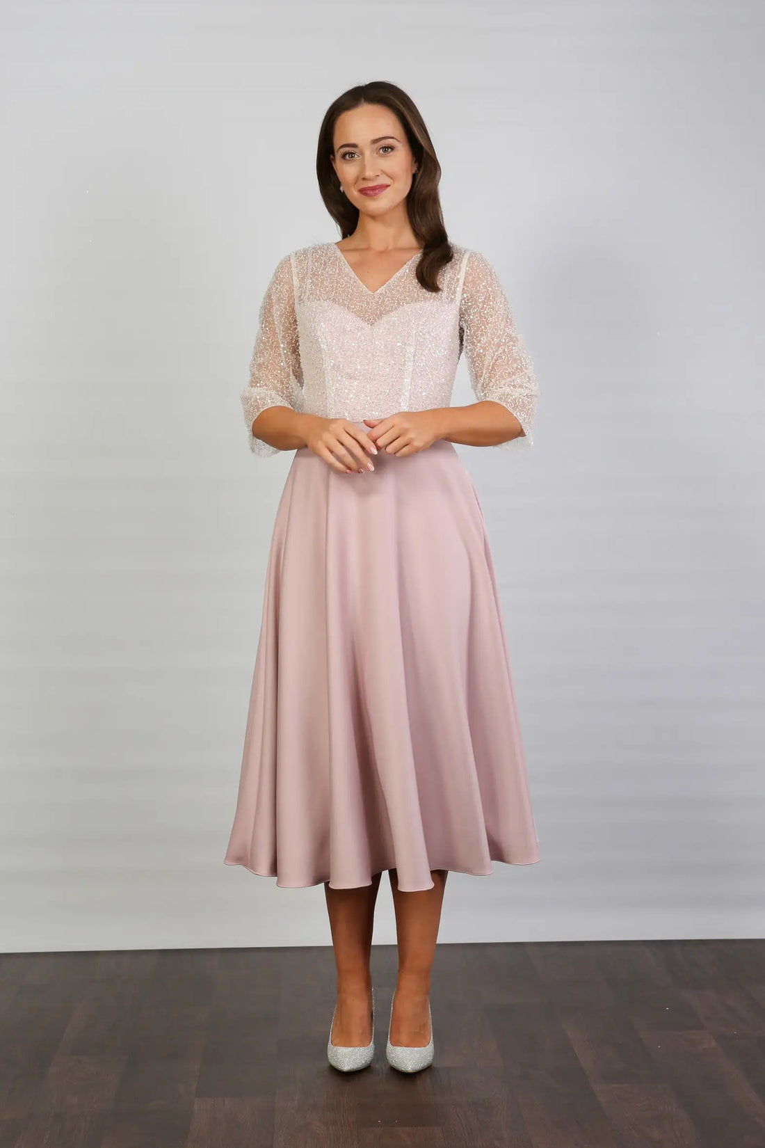 A woman models a blush-coloured, midi-length, beaded special occasion dress with a sweetheart neckline and 3/4 sleeves.