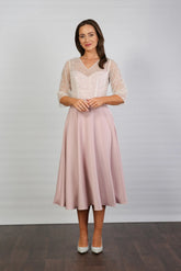 A woman models a blush-coloured, midi-length, beaded special occasion dress with a sweetheart neckline and 3/4 sleeves.