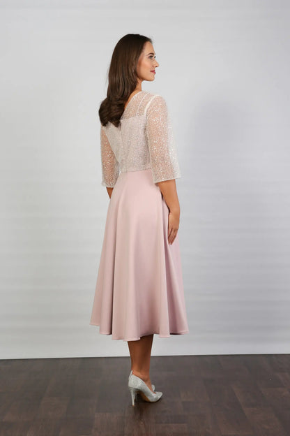 A woman models a blush-coloured, midi-length, beaded special occasion dress with a sweetheart neckline and 3/4 sleeves.