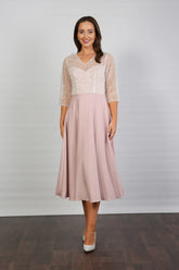 A woman models a blush-coloured, midi-length, beaded special occasion dress with a sweetheart neckline and 3/4 sleeves.