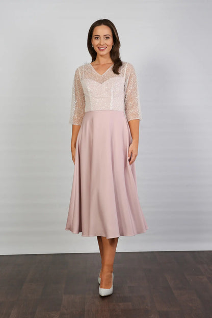 A woman models a blush-coloured, midi-length, beaded special occasion dress with a sweetheart neckline and 3/4 sleeves.