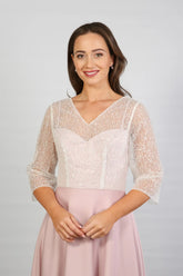 A woman models a blush-coloured, midi-length, beaded special occasion dress with a sweetheart neckline and 3/4 sleeves.