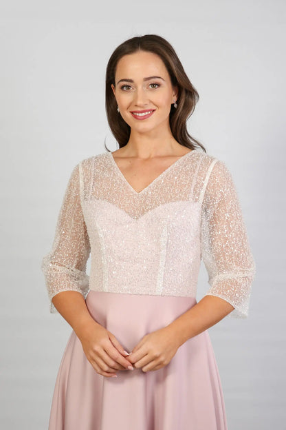 A woman models a blush-coloured, midi-length, beaded special occasion dress with a sweetheart neckline and 3/4 sleeves.
