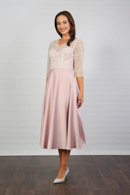 A woman models a blush-coloured, midi-length, beaded special occasion dress with a sweetheart neckline and 3/4 sleeves.