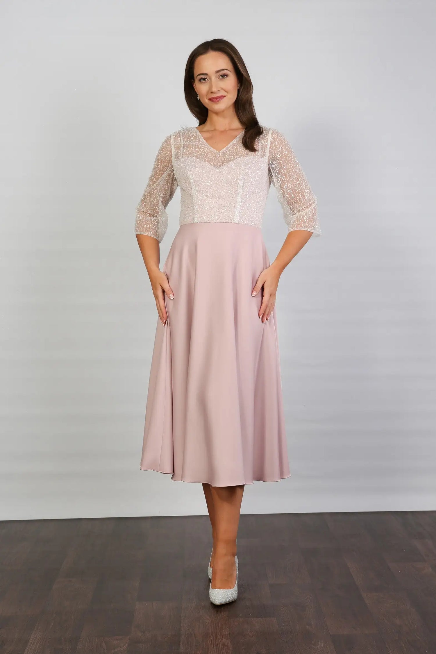A woman models a blush-coloured, midi-length, beaded special occasion dress with a sweetheart neckline and 3/4 sleeves.