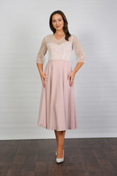 A woman models a blush-coloured, midi-length, beaded special occasion dress with a sweetheart neckline and 3/4 sleeves.