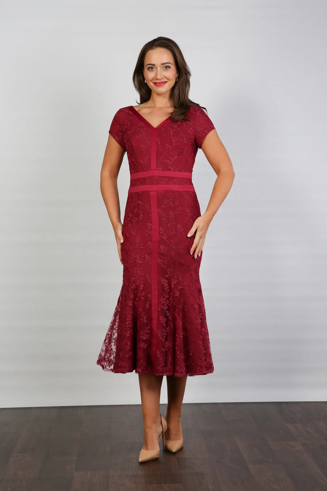 A woman models a short-sleeved, midi-length, red dress with embroidery and a v-neckline. The dress has cap sleeves and a back zip fastening, suitable for formal summer events.