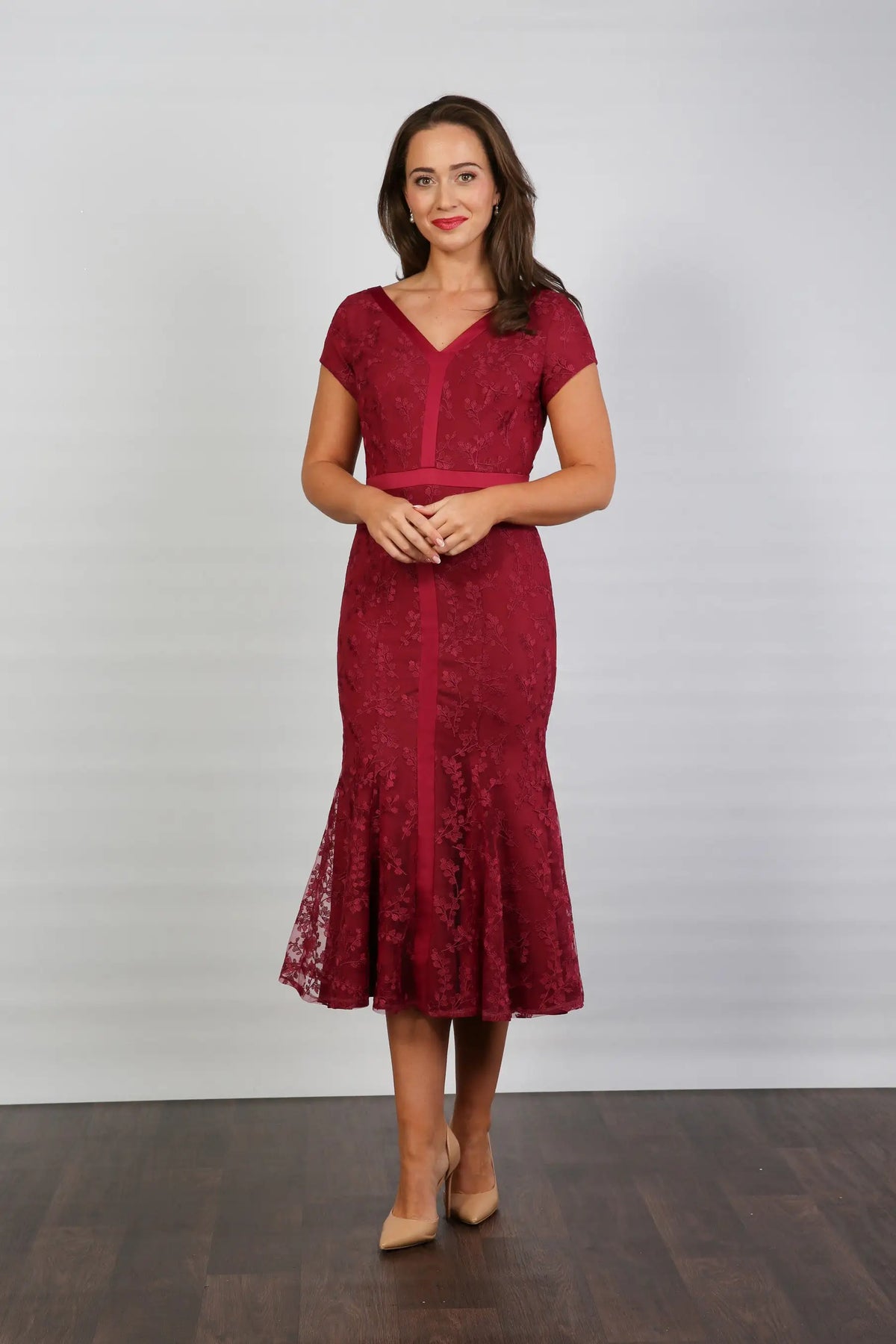 A woman models a short-sleeved, midi-length, red dress with embroidery and a v-neckline. The dress has cap sleeves and a back zip fastening, suitable for formal summer events.