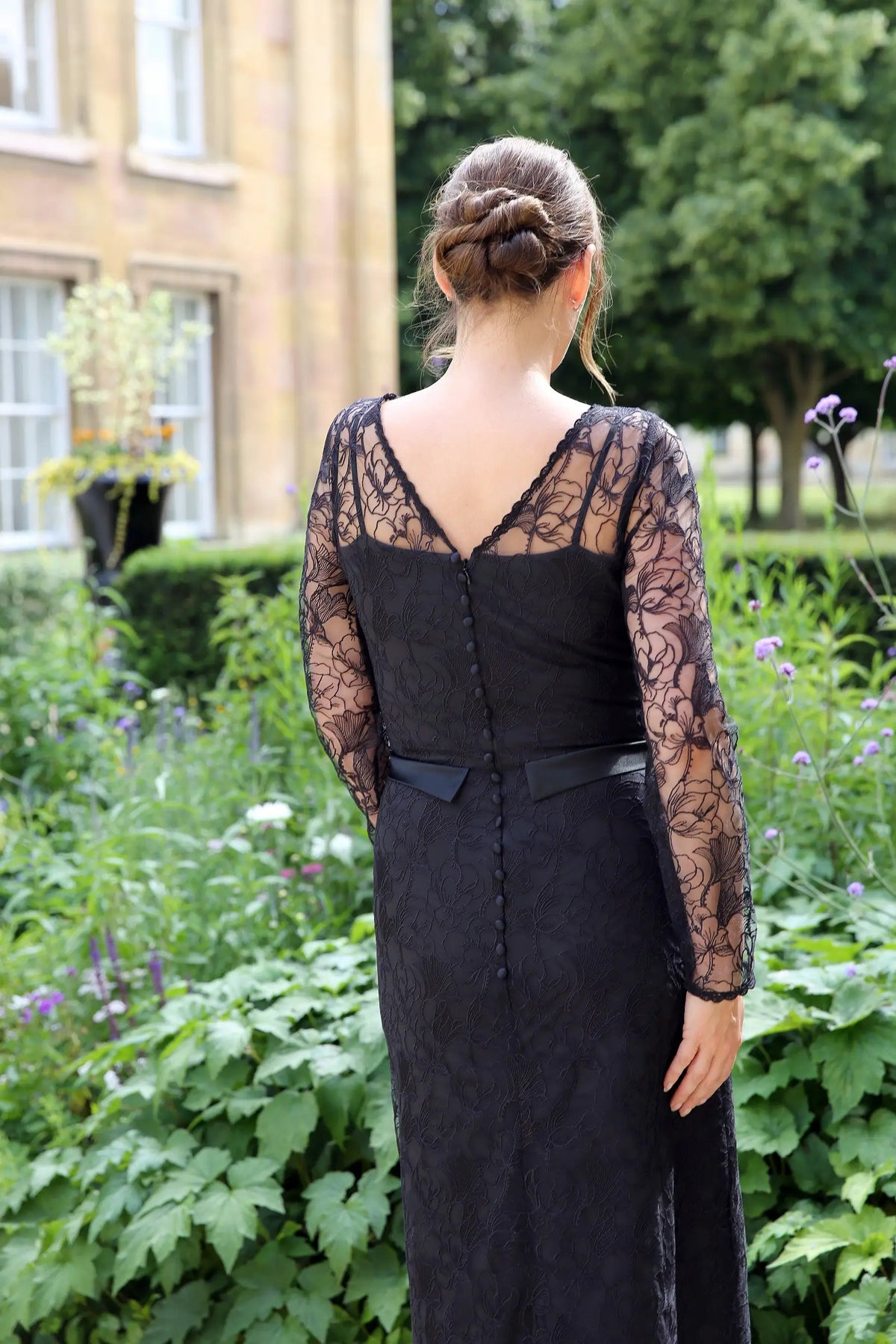 A woman wearing a black ankle-length evening dress with long sleeves and textured lace detailing.
