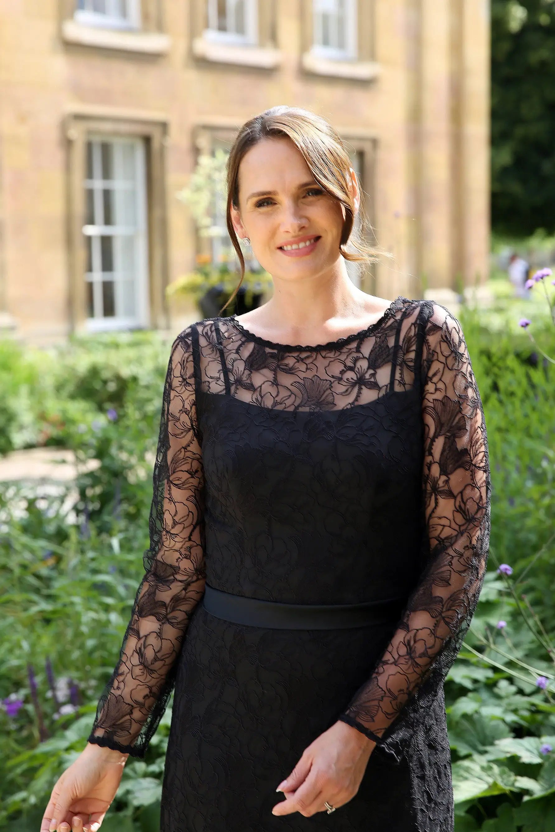 A woman wearing a black ankle-length evening dress with long sleeves and textured lace detailing.