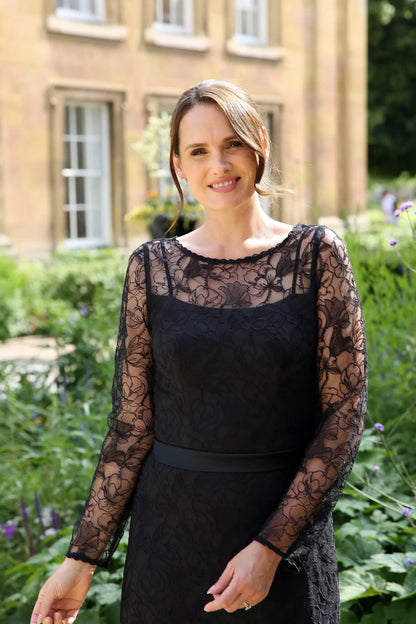 A woman wearing a black ankle-length evening dress with long sleeves and textured lace detailing.