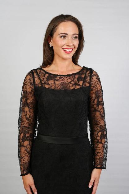 A woman wearing a black ankle-length evening dress with long sleeves and textured lace detailing.