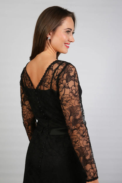 A woman wearing a black ankle-length evening dress with long sleeves and textured lace detailing.