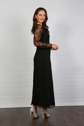 A woman wearing a black ankle-length evening dress with long sleeves and textured lace detailing.