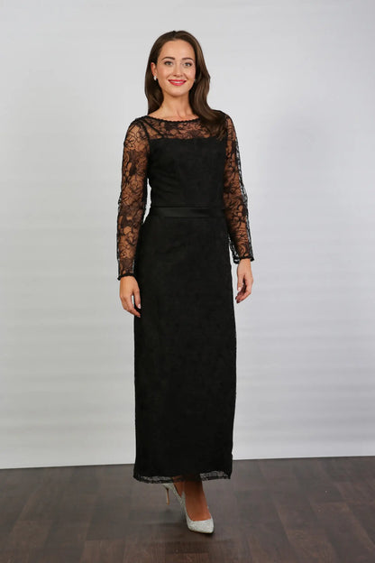 A woman wearing a black ankle-length evening dress with long sleeves and textured lace detailing.
