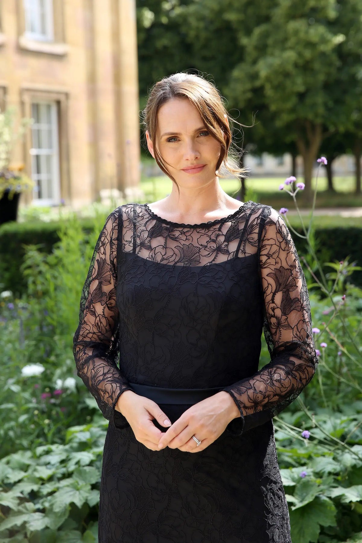 A woman wearing a black ankle-length evening dress with long sleeves and textured lace detailing.