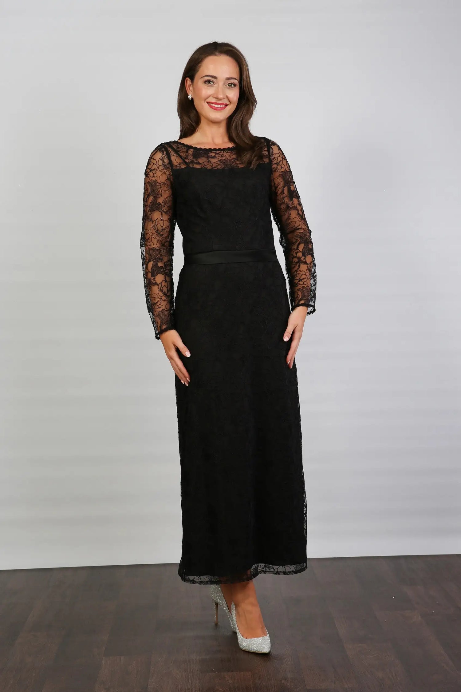 A woman wearing a black ankle-length evening dress with long sleeves and textured lace detailing.