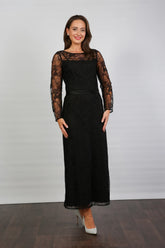 A woman wearing a black ankle-length evening dress with long sleeves and textured lace detailing.