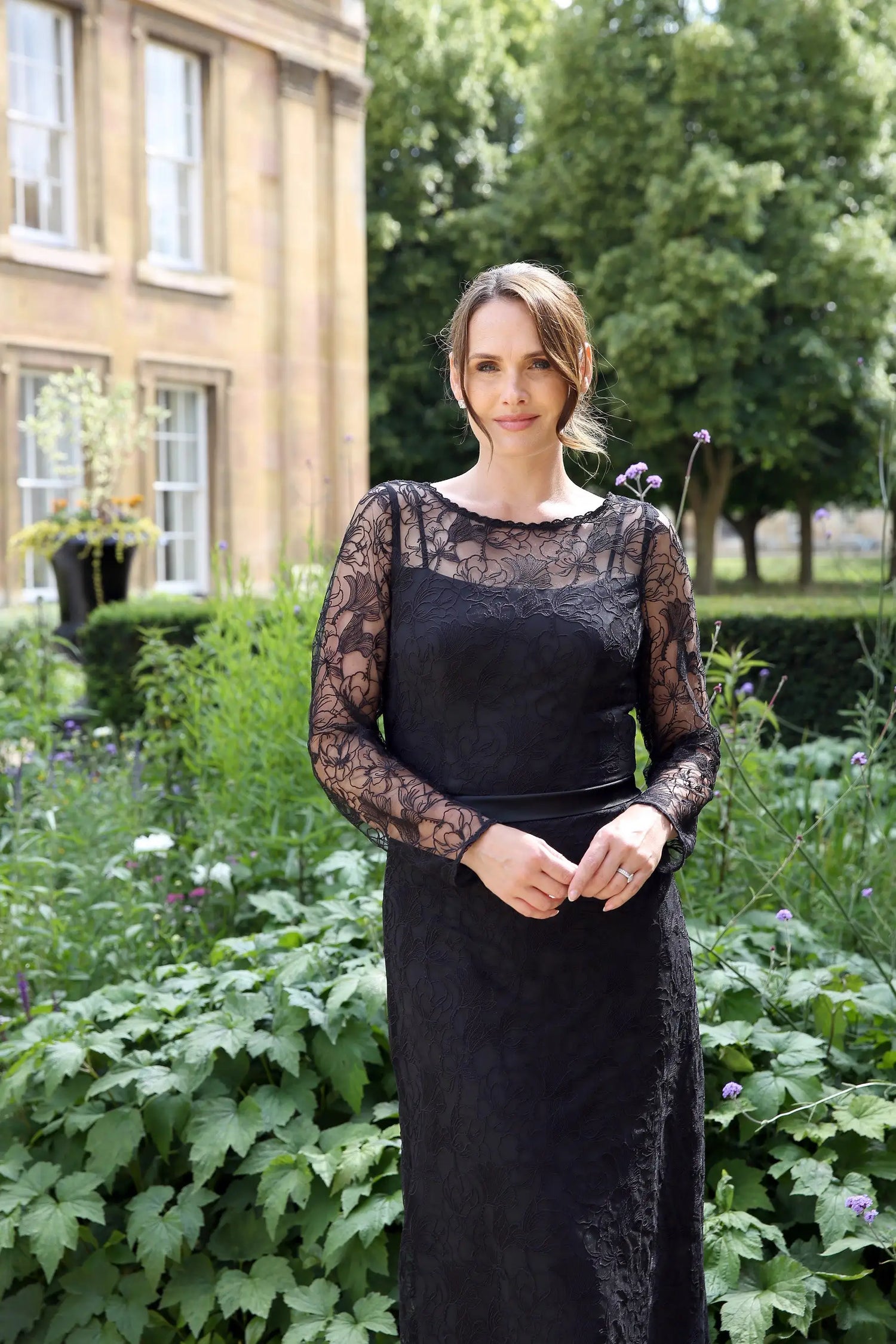 A woman wearing a black ankle-length evening dress with long sleeves and textured lace detailing.