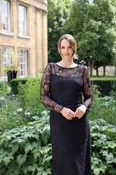 A woman wearing a black ankle-length evening dress with long sleeves and textured lace detailing.