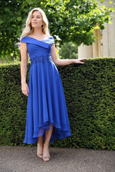 A woman wearing an electric blue flowing chiffon dress with a pleated satin Bardot neckline and a high-low hem.