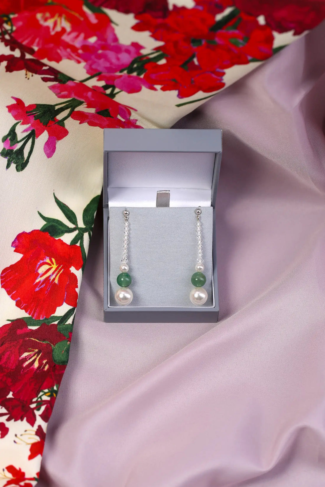A pair of natural Aventurine and Pearl Drop Earrings displayed in an open keepsake box, with the earrings hanging on a floral patterned surface.
