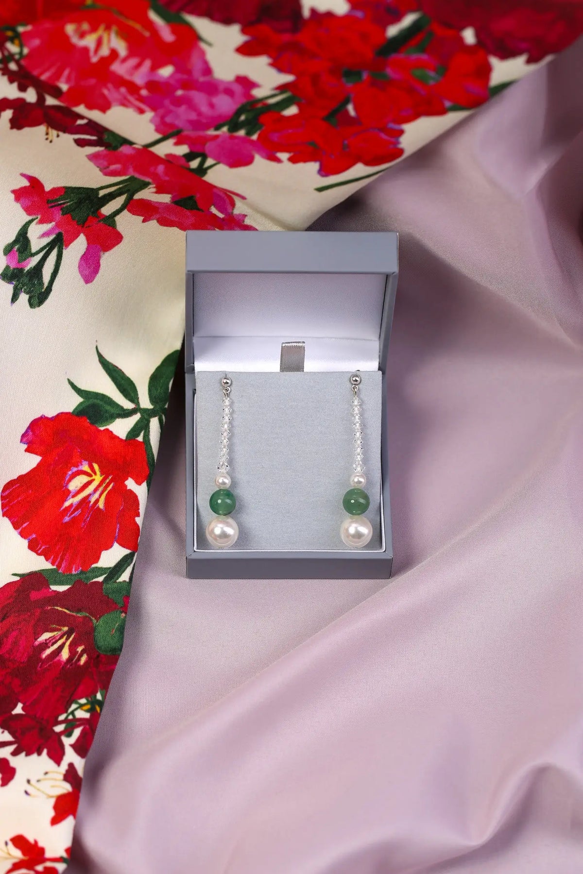 A pair of natural Aventurine and Pearl Drop Earrings displayed in an open keepsake box, with the earrings hanging on a floral patterned surface.