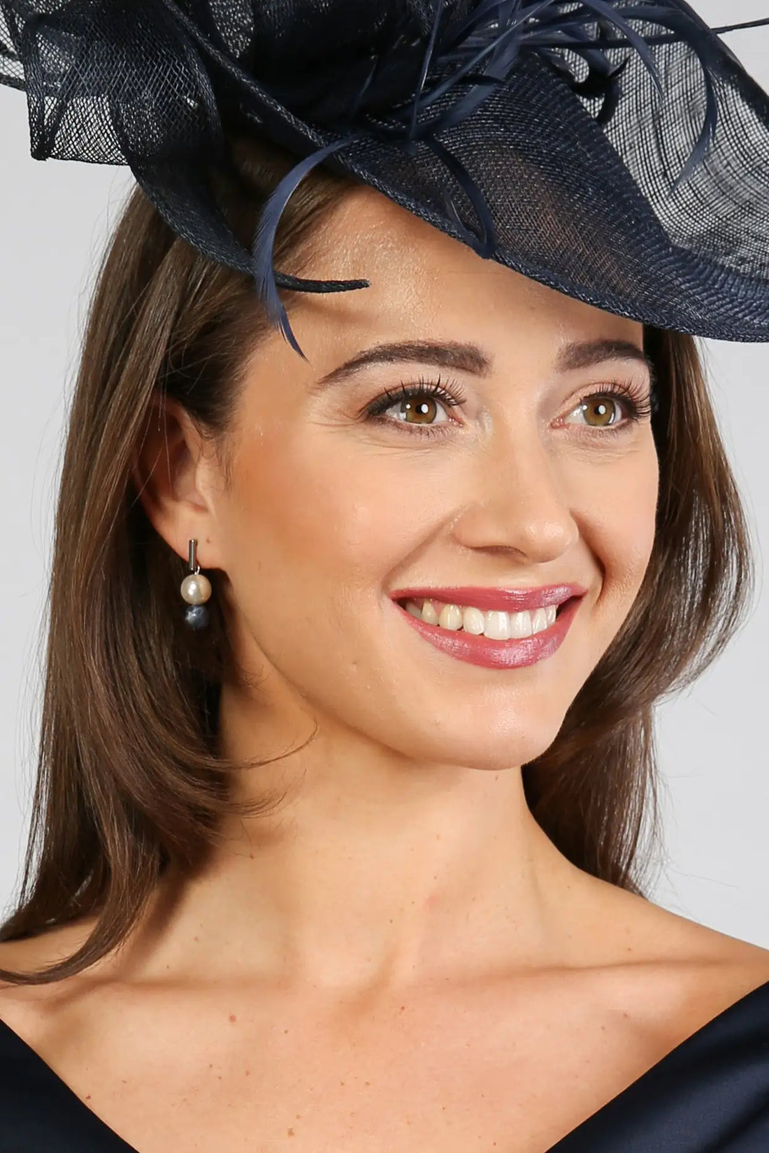 A woman wearing navy and white sodalite and pearl drop earrings with a smile on her face.