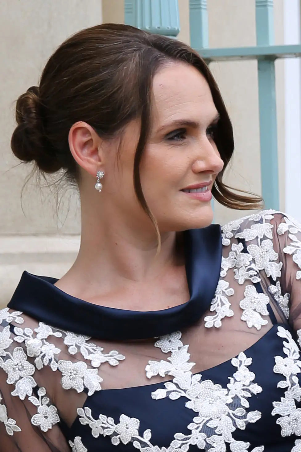 A close-up image of a woman wearing pearl diamante flower drop earrings with a navy dress.