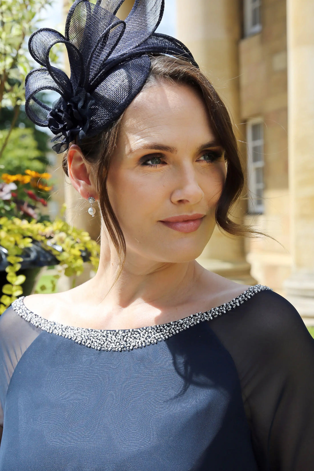 A close-up image of a woman wearing pearl diamante flower drop earrings with a navy dress.