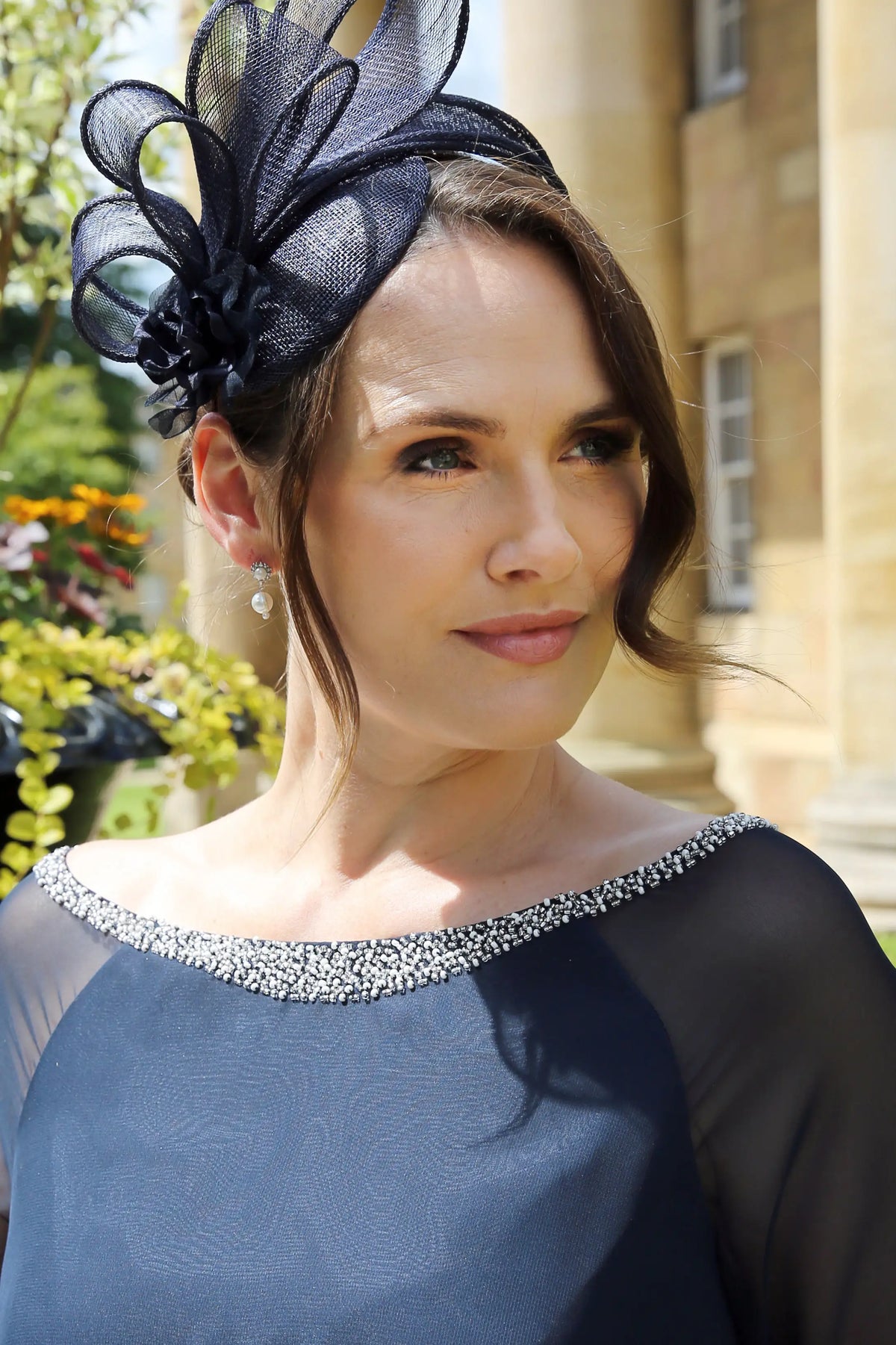 A close-up image of a woman wearing pearl diamante flower drop earrings with a navy dress.