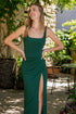 Woman in a green dress standing outdoors with plants and furniture in the background