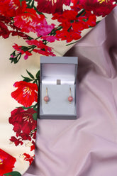 A pair of gold-coloured earrings with round cream pearls and mauve rhodonite beads, presented in a box with a floral patterned fabric background.