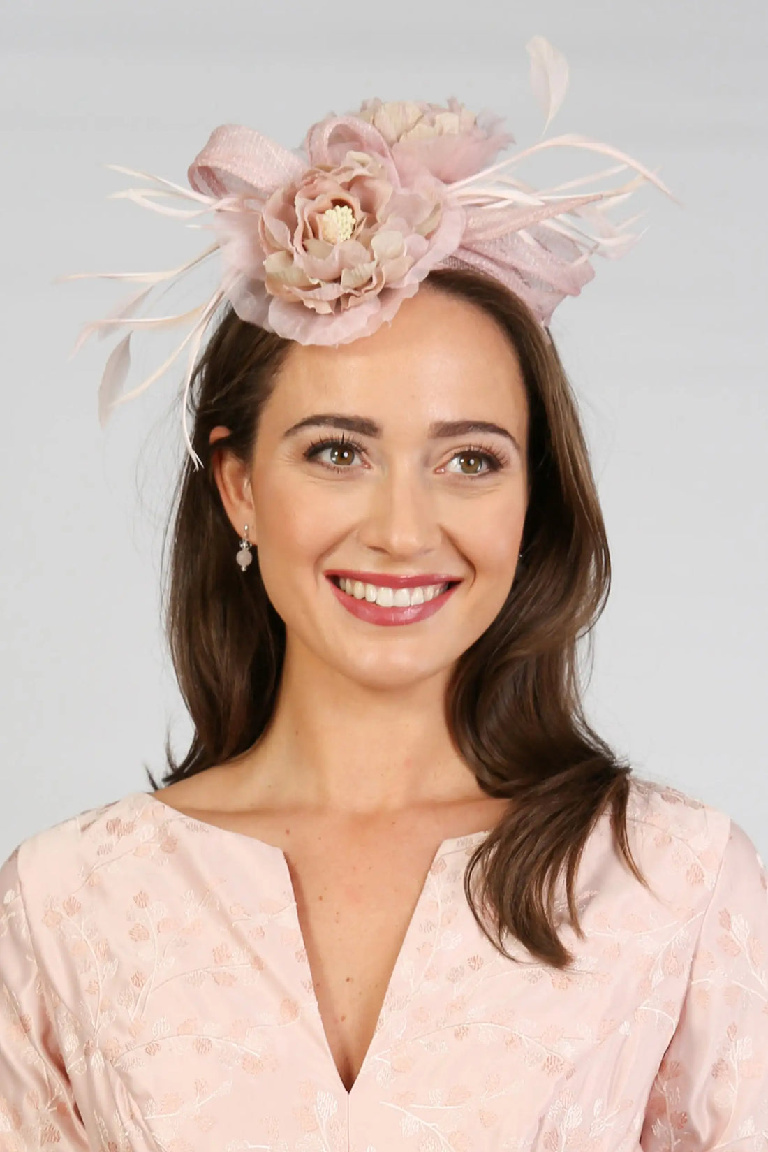 A woman wearing a pink floral fascinator with a satin and chiffon flower design.