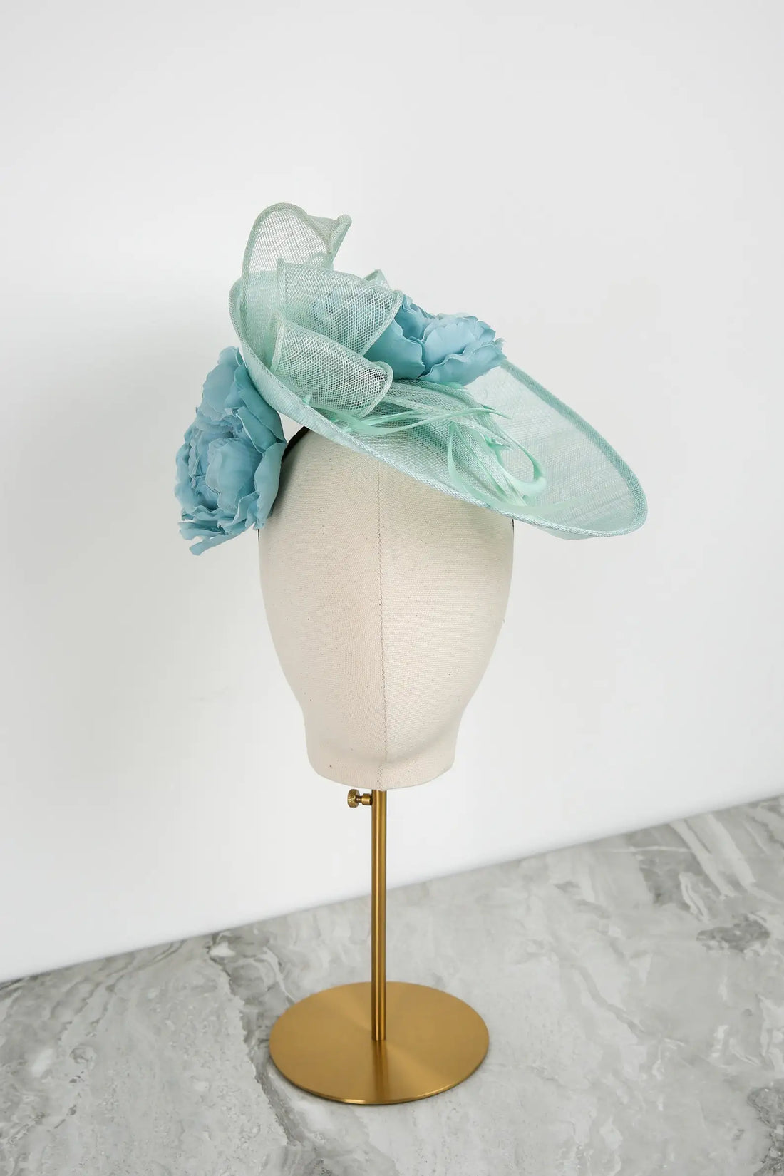 Light blue and green decorative hat on a mannequin head against a white background