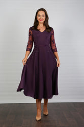 A woman models a midi length blackberry-coloured occasion wear dress with tulle sleeves and floral appliques.