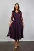 A woman models a midi length blackberry-coloured occasion wear dress with tulle sleeves and floral appliques.