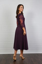 A woman models a midi length blackberry-coloured occasion wear dress with tulle sleeves and floral appliques.