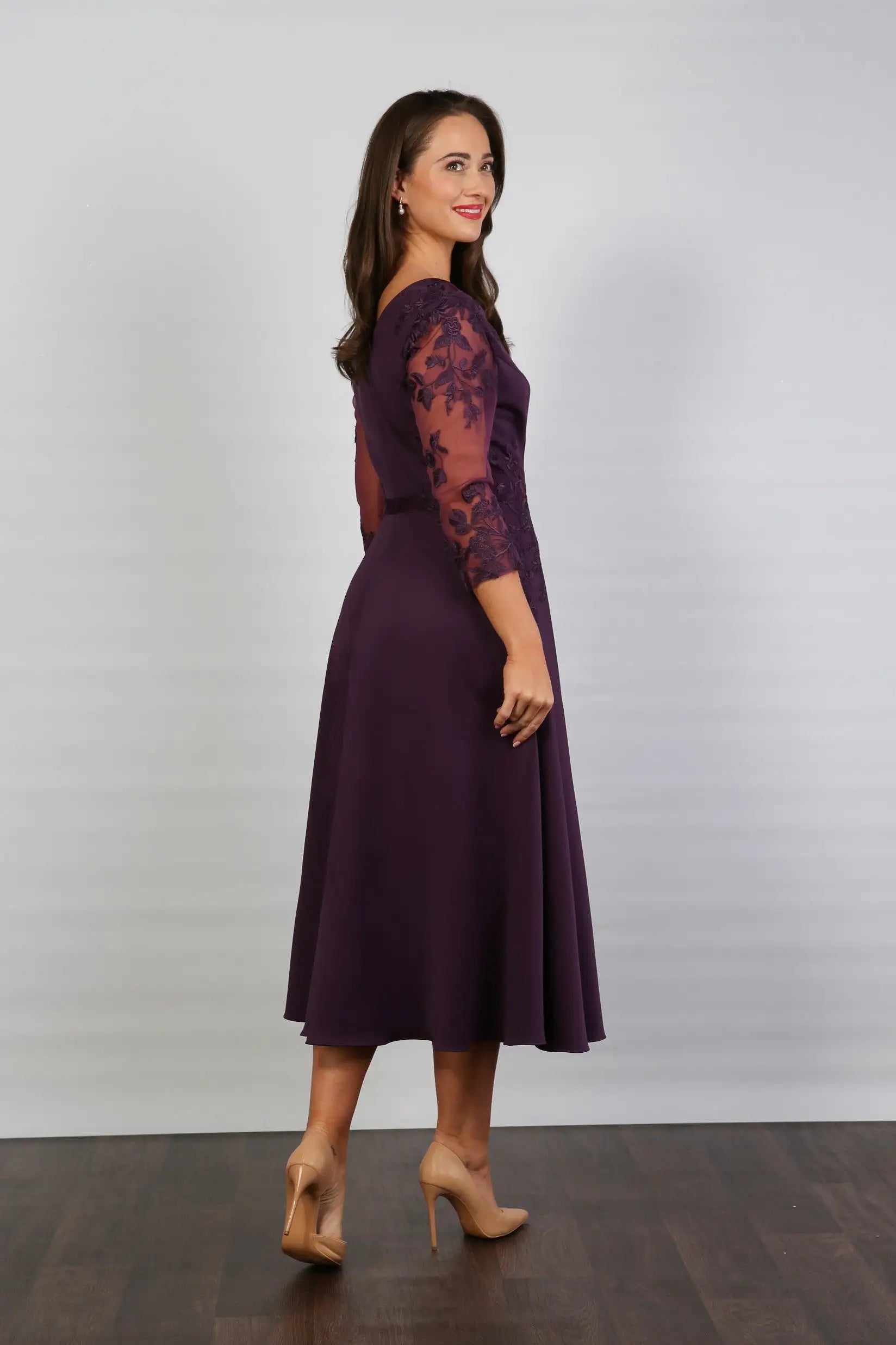 A woman models a midi length blackberry-coloured occasion wear dress with tulle sleeves and floral appliques.