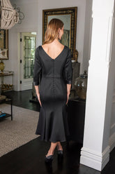 Woman wearing a black dress standing in a room with a mirror and decor.