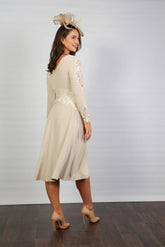 A woman wearing a long sleeve, midi length Almond dress with embroidery detail at the waistline and sleeves.