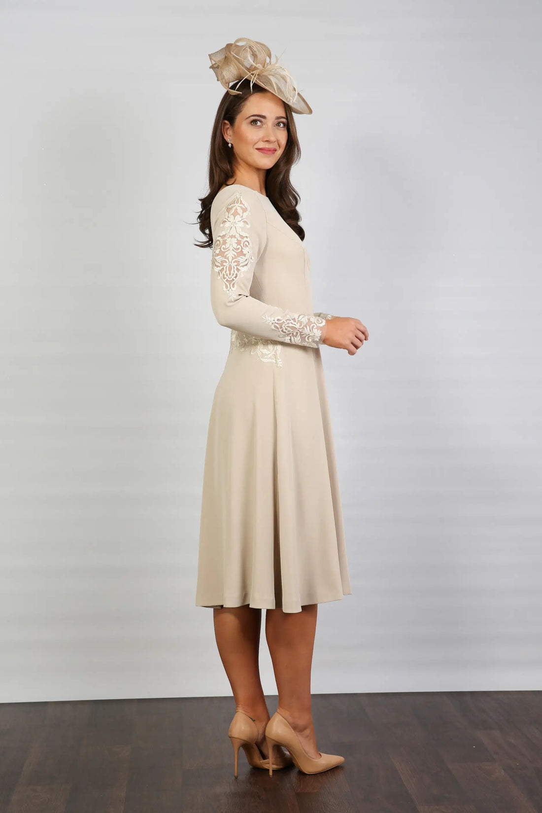 A woman wearing a long sleeve, midi length Almond dress with embroidery detail at the waistline and sleeves.
