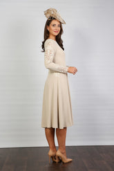A woman wearing a long sleeve, midi length Almond dress with embroidery detail at the waistline and sleeves.