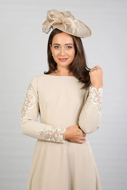 A woman wearing a long sleeve, midi length Almond dress with embroidery detail at the waistline and sleeves.