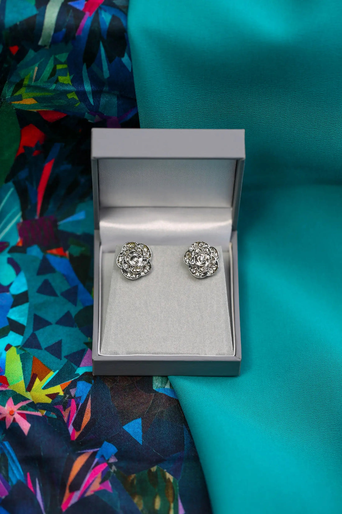 Silver earrings in a box on a colourful fabric background.
